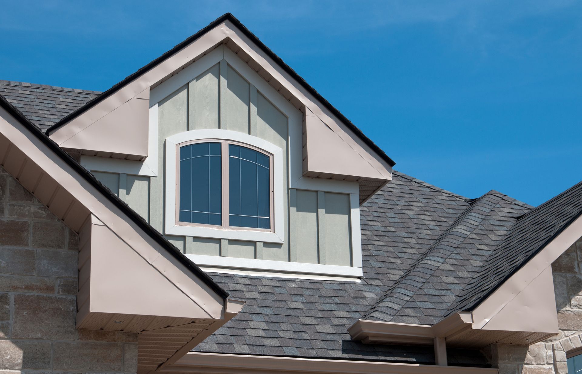 Dormer window with arched top on a house with gray shingles and blue sky.