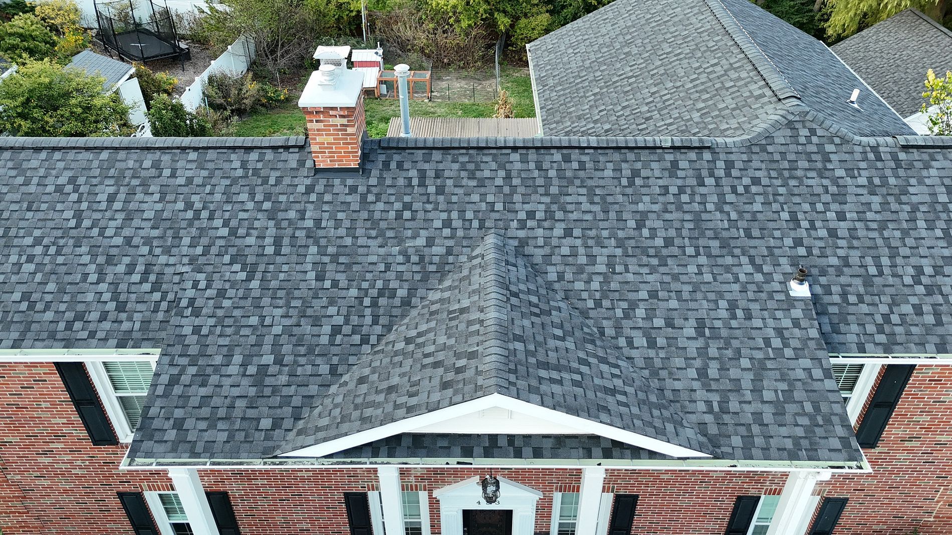 Overhead view of a brick house with a dark gray shingle roof, chimney, and porch.