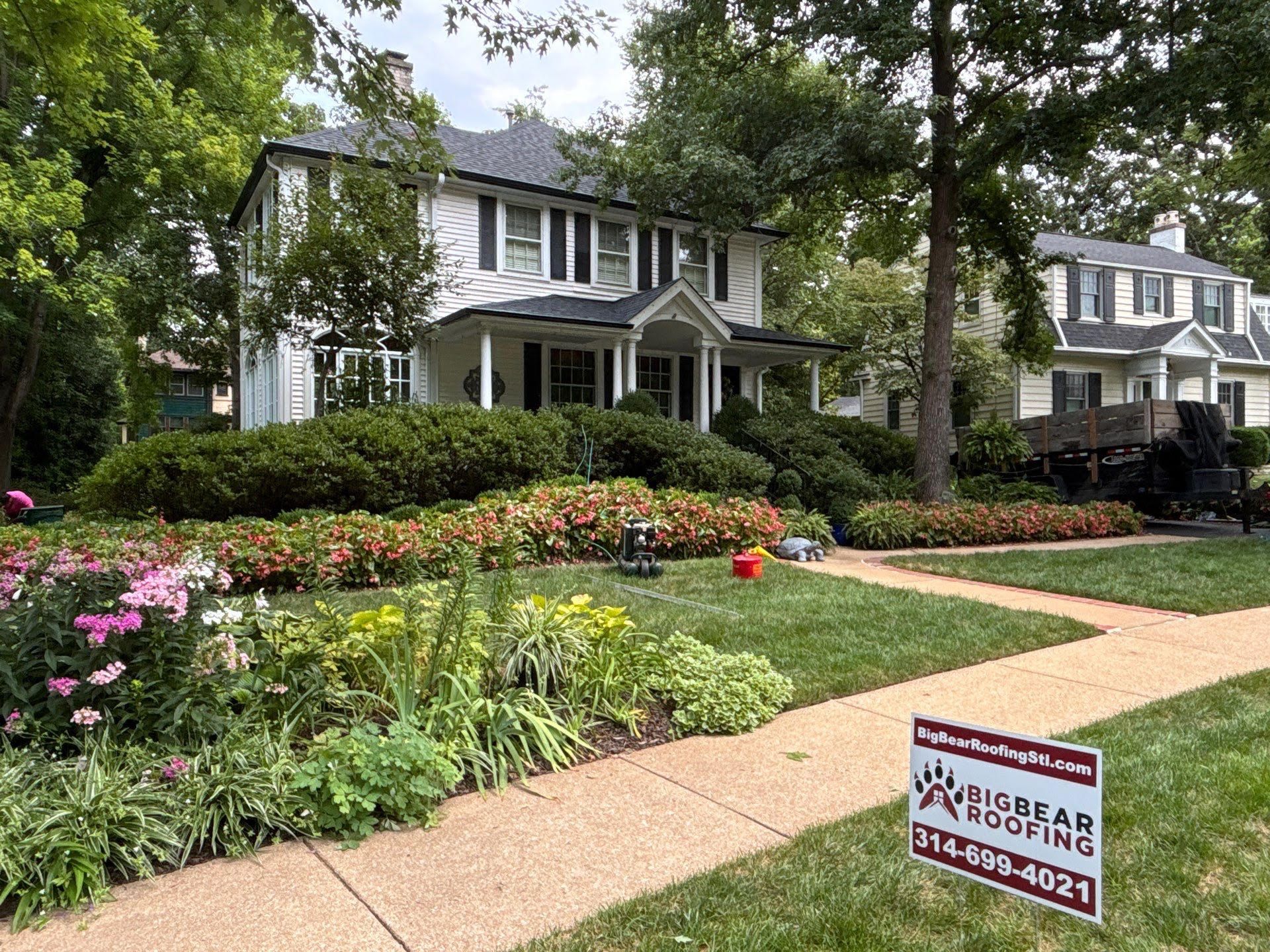 White house with black roof and Big Bear Roofing sign in front yard.