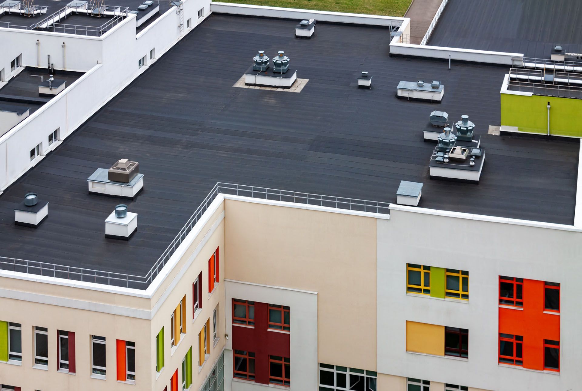 A flat, black roof of a building with various rooftop units and colorful windows.
