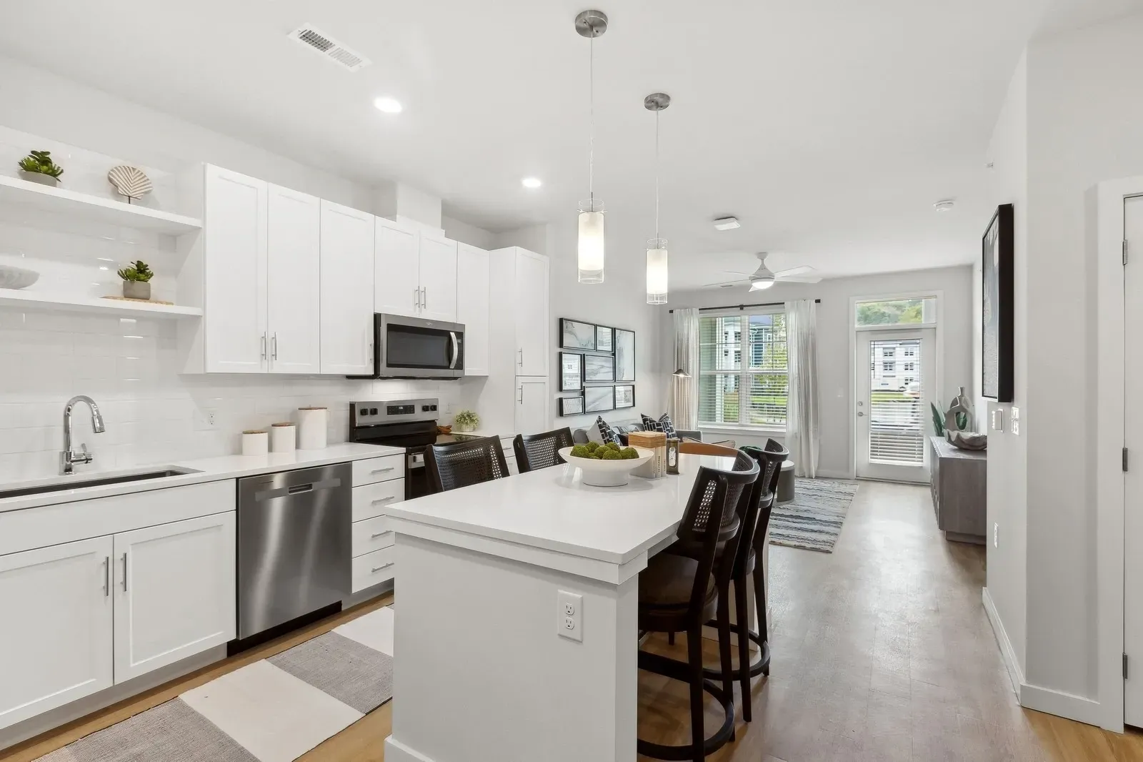 Open-concept kitchen with white cabinets, island seating, and stainless steel appliances.