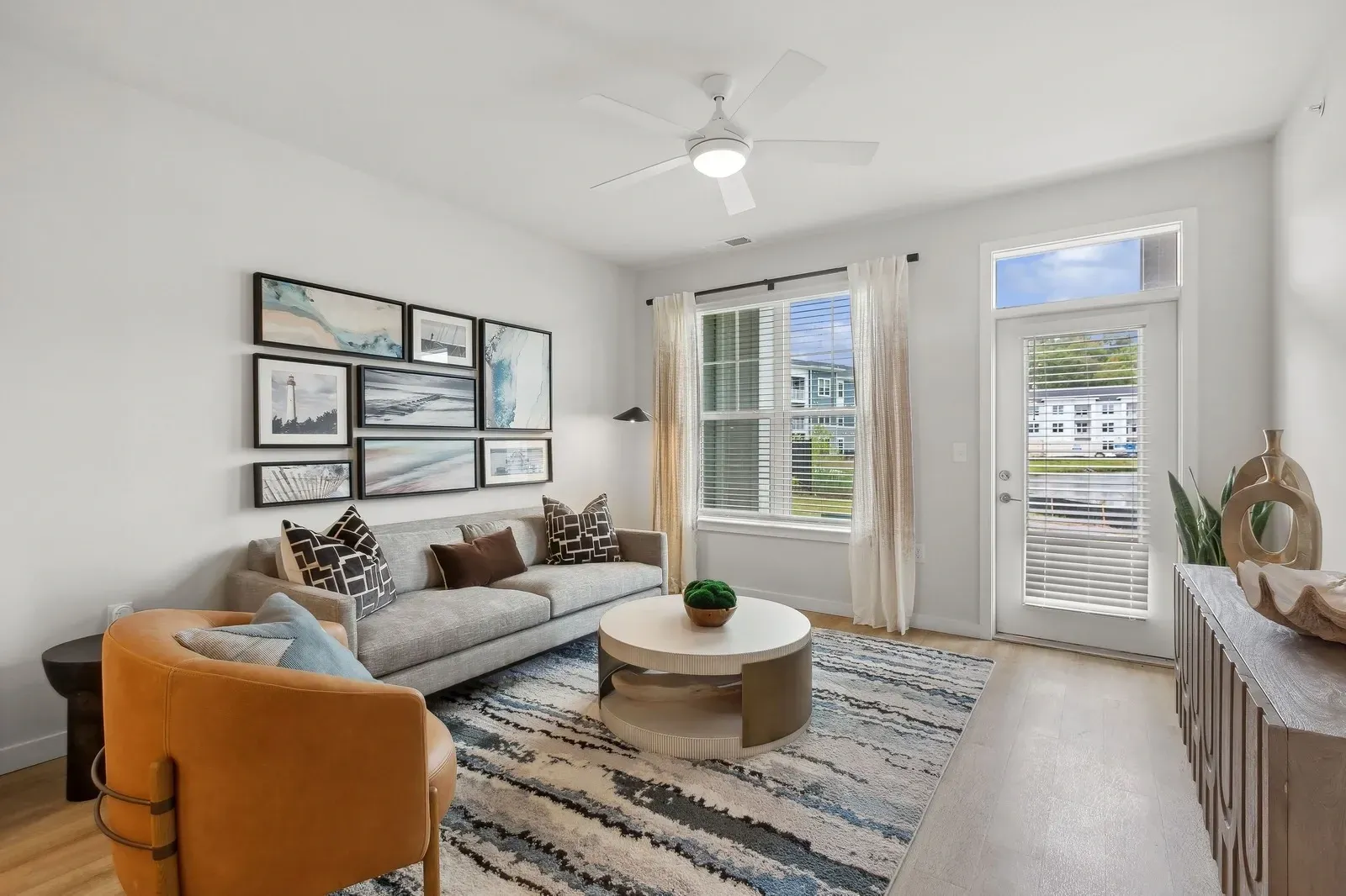 Bright apartment living room with a gray sofa, mustard chair, wall art, and a large window.