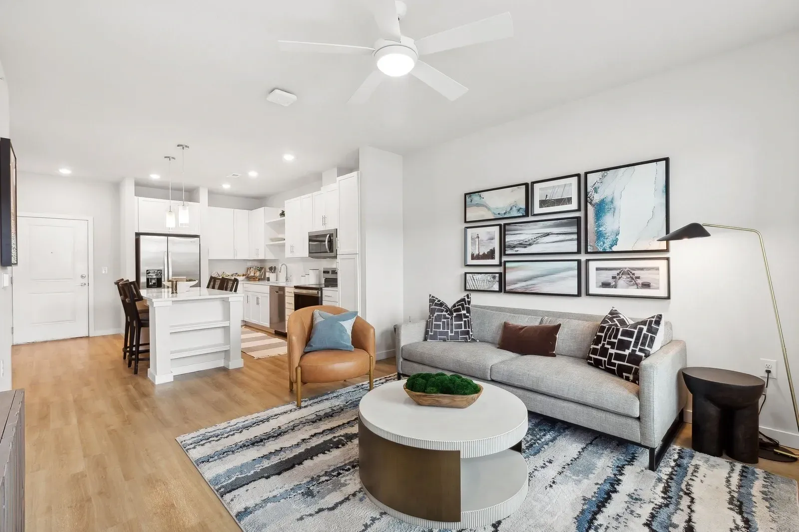 Open-concept living room and kitchen with white cabinets, island, sofa, and wall art.
