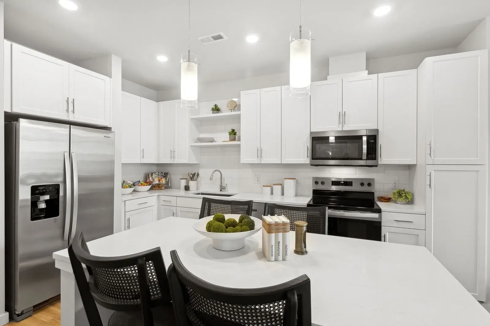 Modern white kitchen in an apartment with stainless steel fridge, microwave, range, and island.