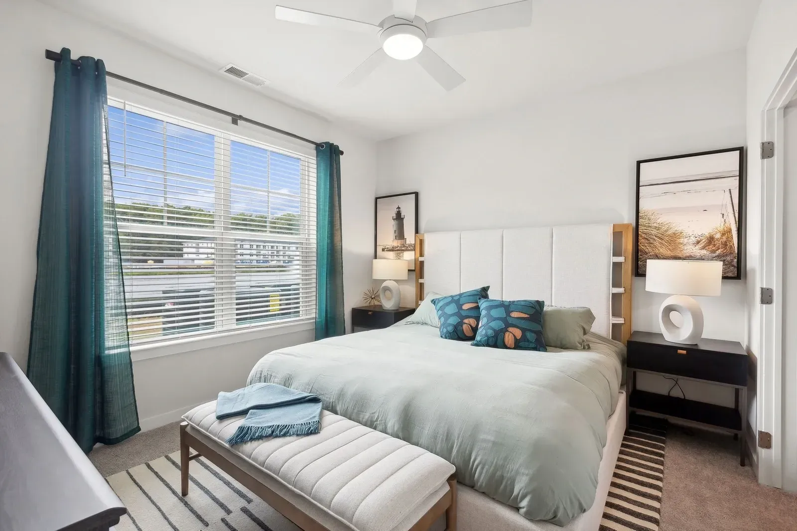 Bedroom with a queen bed, teal drapes, ceiling fan, nightstands, and a large window with blinds.