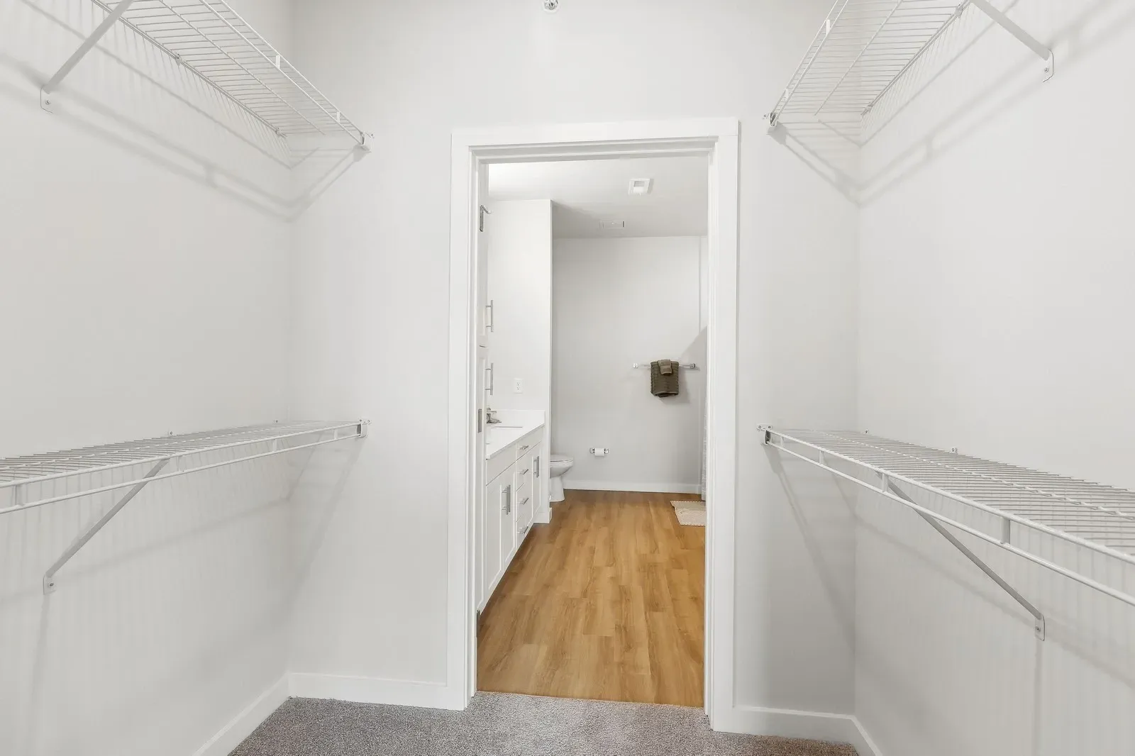 Bright walk-in closet with white wire shelving on both sides and doorway to the bathroom.