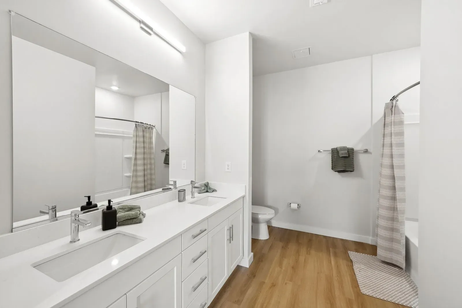 Bright modern bathroom with a double-sink vanity, large mirror, and shower/tub with a striped curtain.
