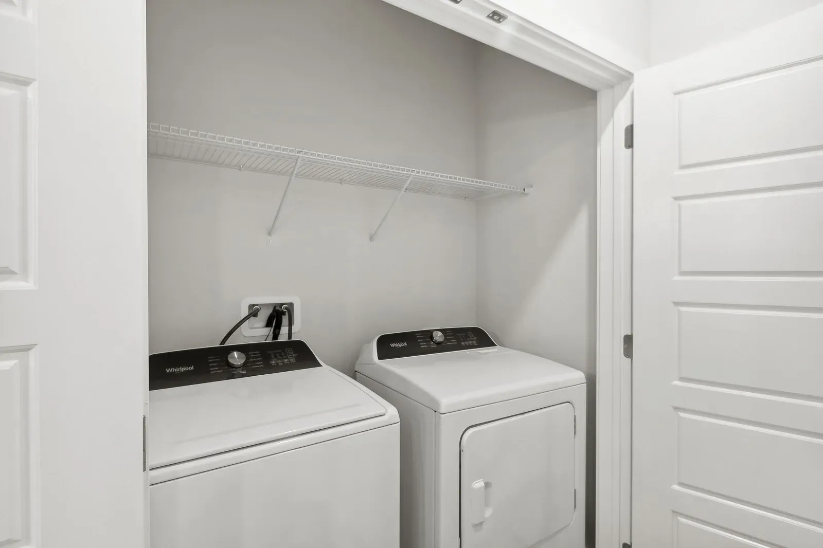 In-unit laundry closet with two side-by-side laundry machines and a wire shelf.
