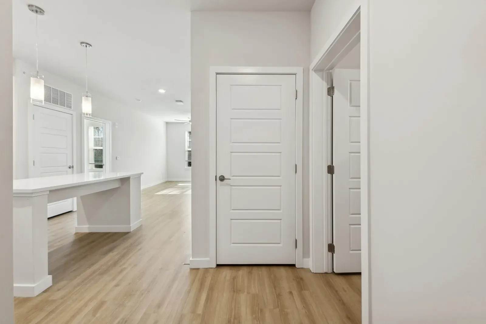 Bright apartment interior with white walls, an island in the kitchen, and pendant lights.
