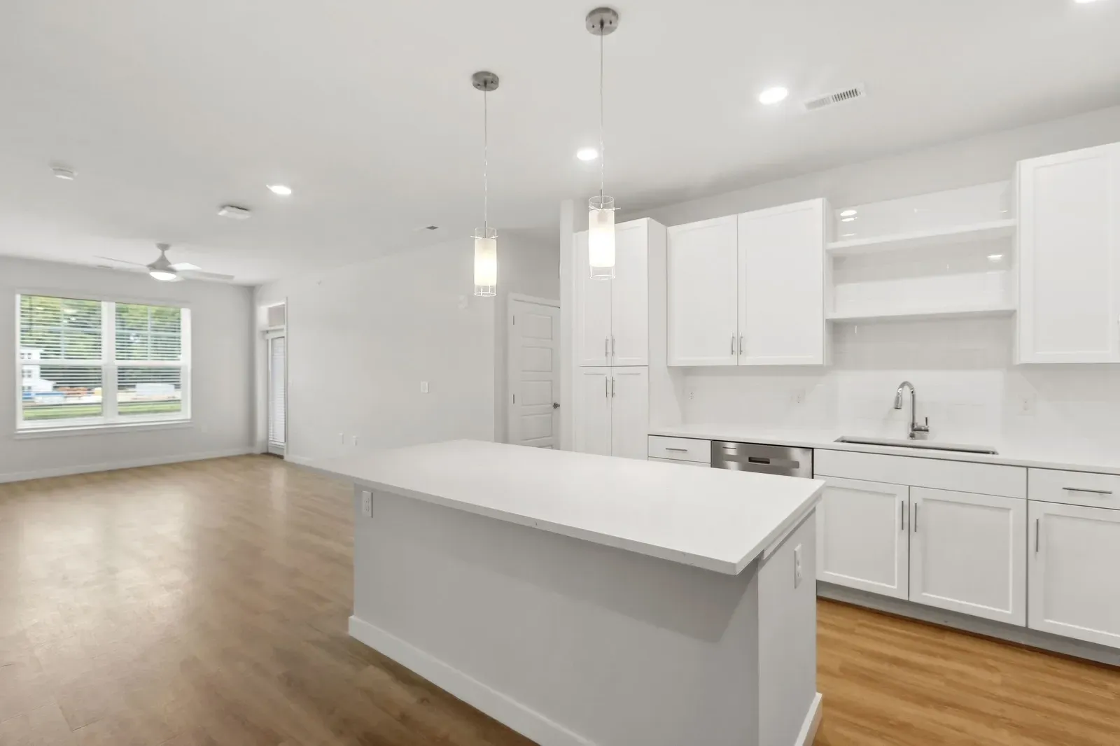 Bright white kitchen with an island, pendant lights, white cabinets, and hardwood floors.
