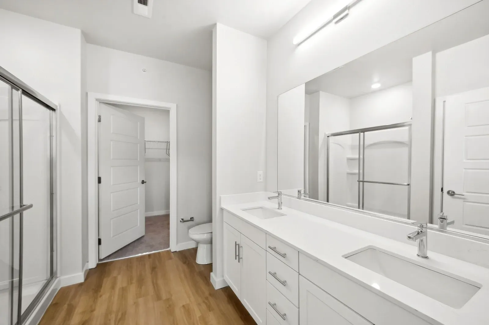Bright white bathroom with a double-sink vanity, large mirror, and a glass-enclosed shower.