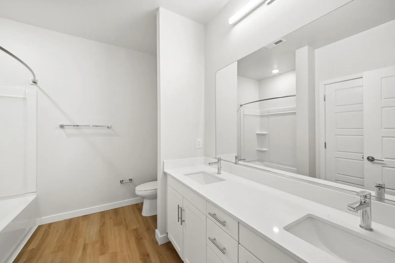 Modern white bathroom with a double vanity, large mirror, and tub/shower.