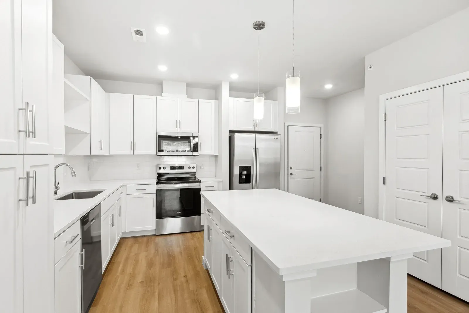 Bright modern white kitchen with an island, stainless steel appliances, and light wood flooring.