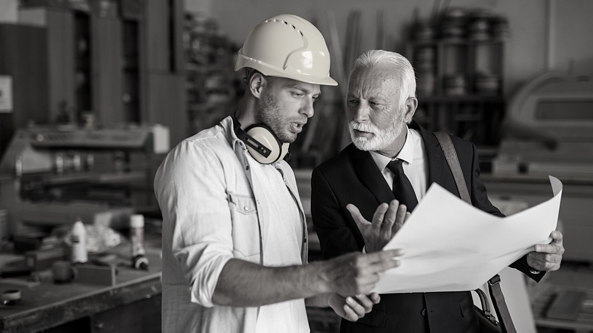 Two men are looking at a blueprint in a factory.