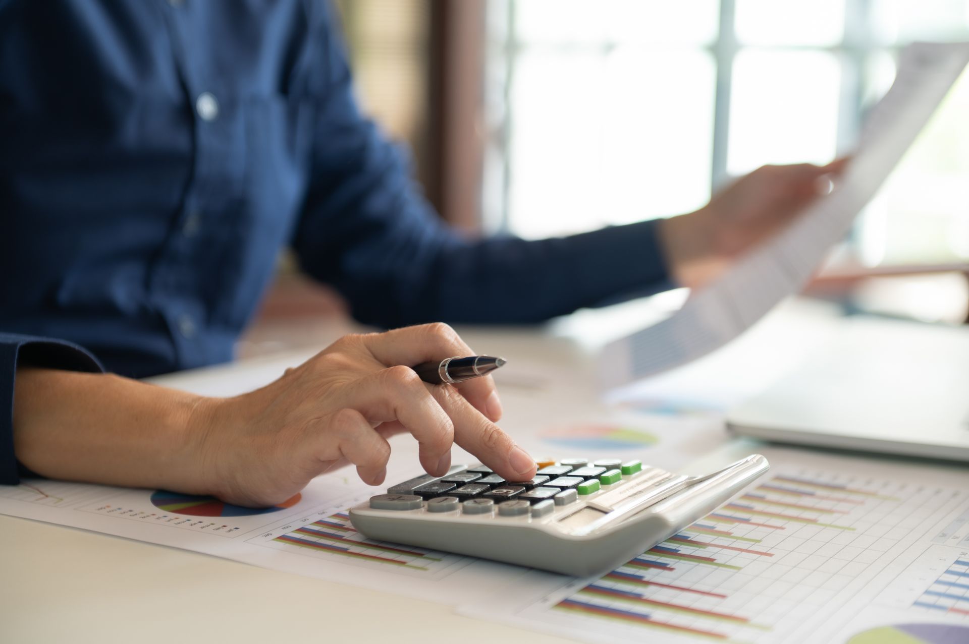 A person is using a calculator while holding a pen.
