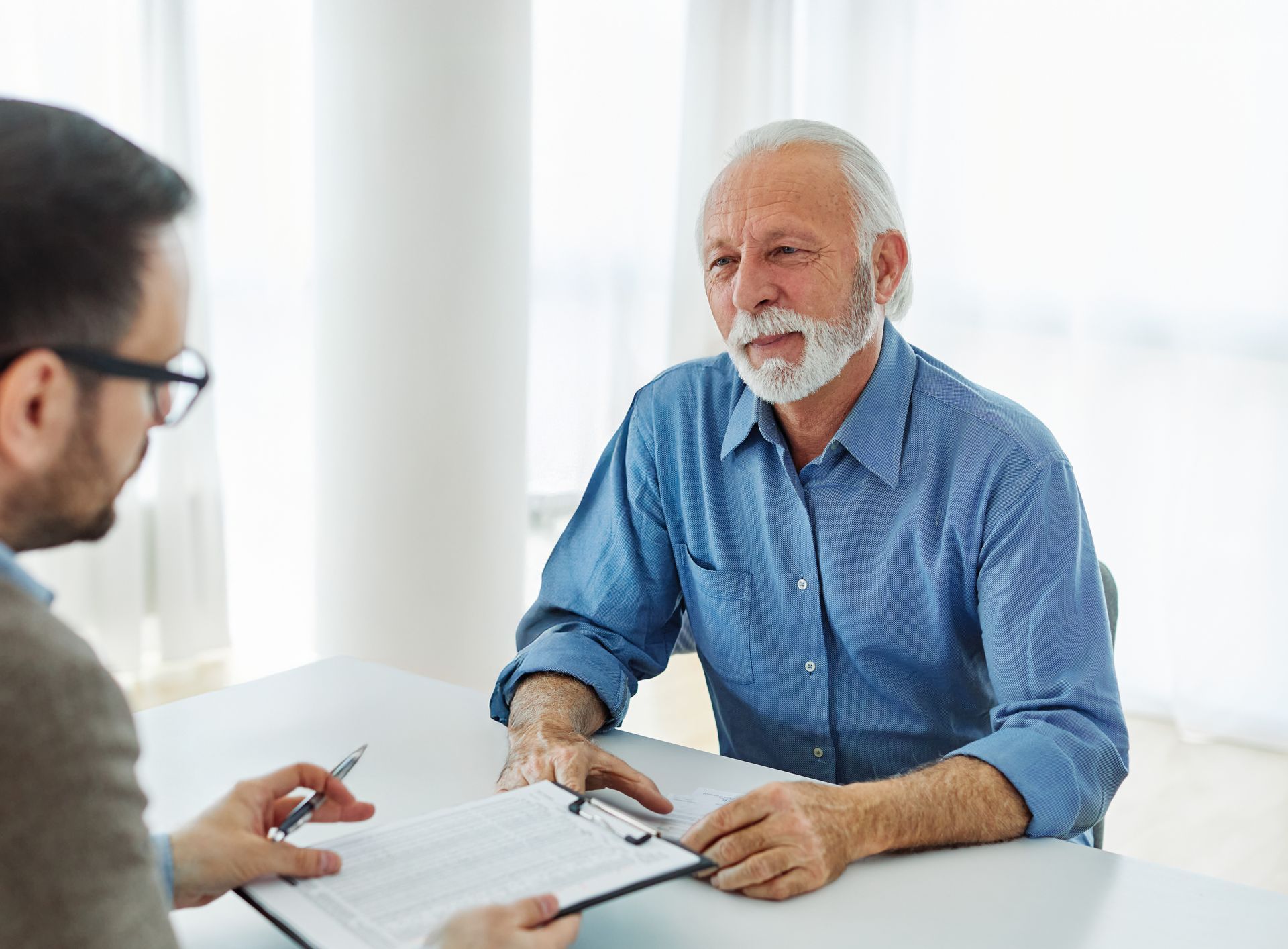 An older man is sitting at a table talking to a younger man.