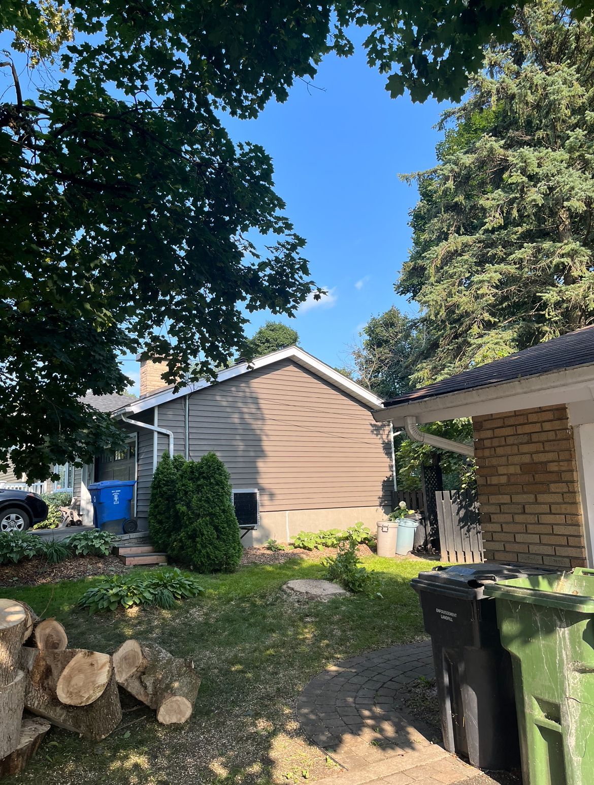 Vue sur le jardin : maison au bardage marron, pelouse verte, arbres et ciel bleu.