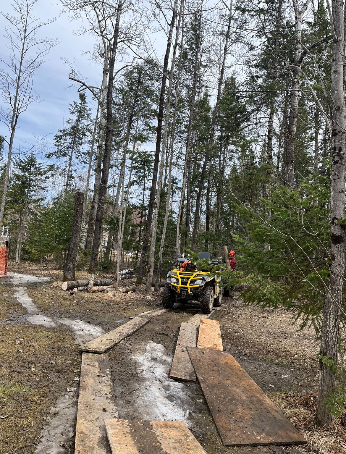 Un quad sur un sentier boueux en forêt, des planches posées au sol pour améliorer l'adhérence.