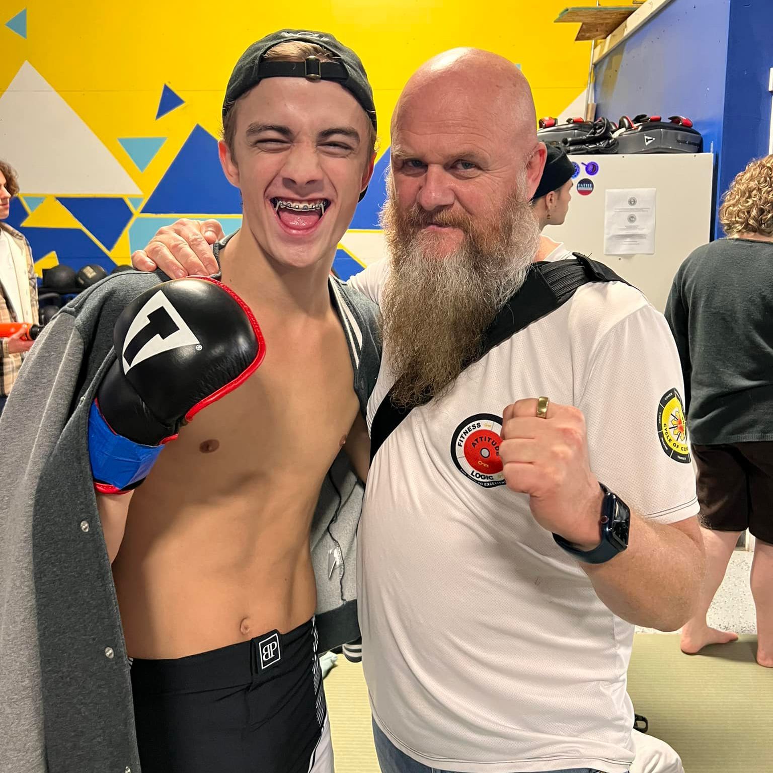 A man with a beard is standing next to a young man wearing boxing gloves with the letter t on them