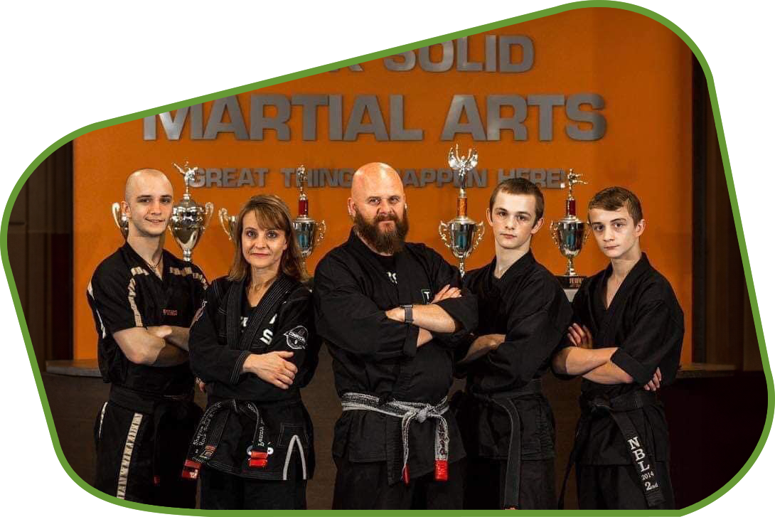a group of martial arts students pose in front of a solid martial arts sign