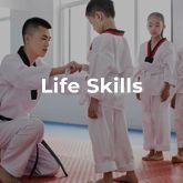 A man is kneeling down next to a young boy in a taekwondo class.