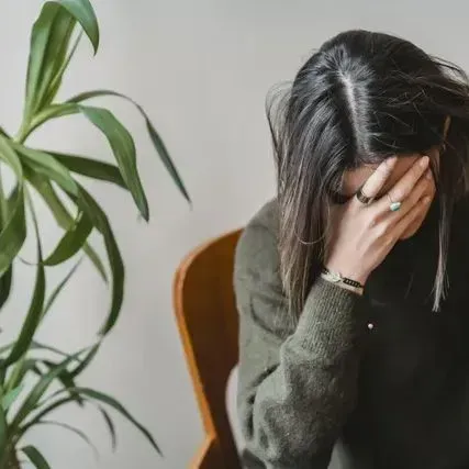 A woman is sitting in a chair covering her face with her hand.