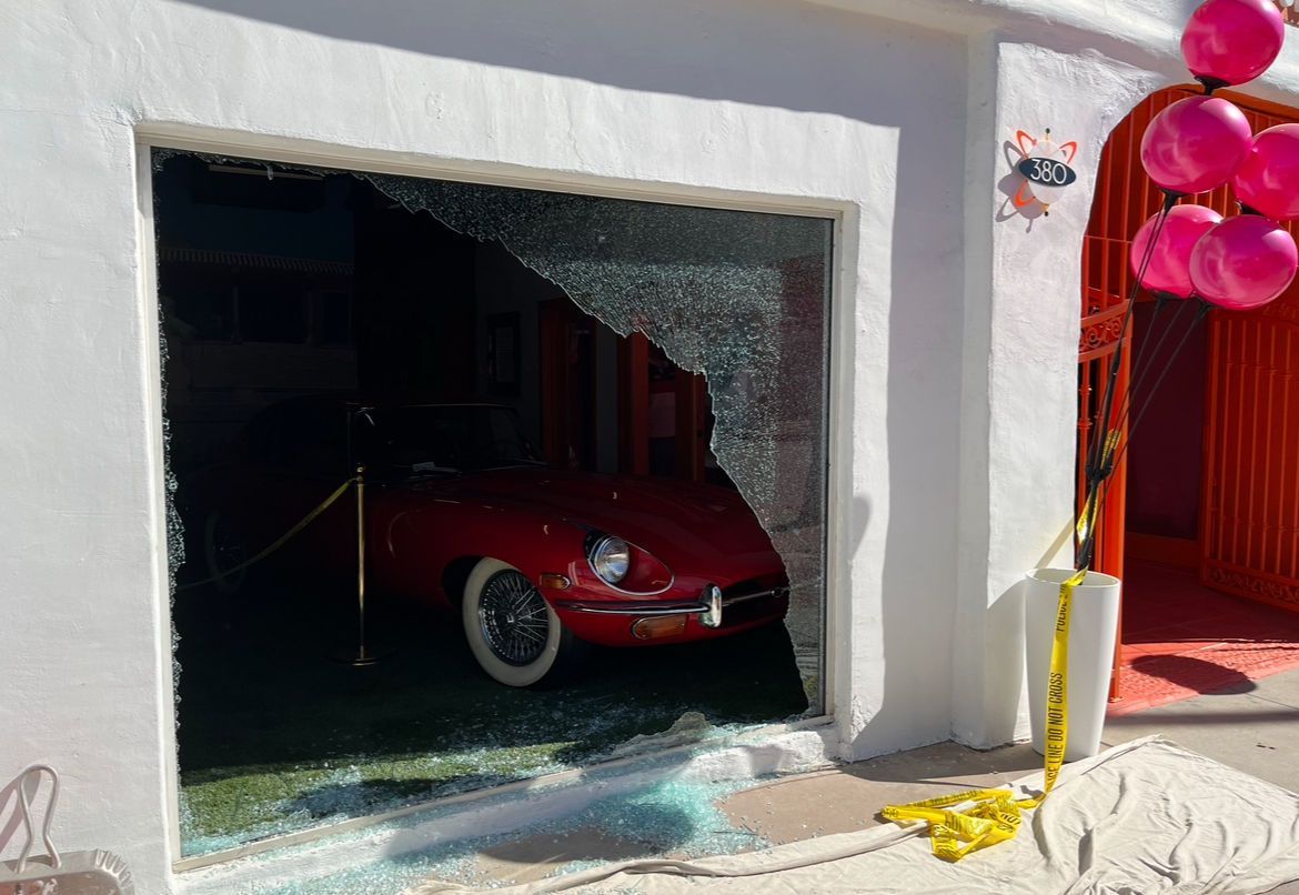 A red car is parked in a garage with a broken glass door.