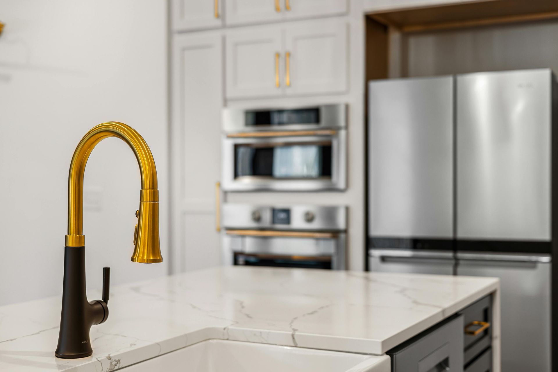 Gold faucet on white countertop in modern kitchen with stainless steel appliances.