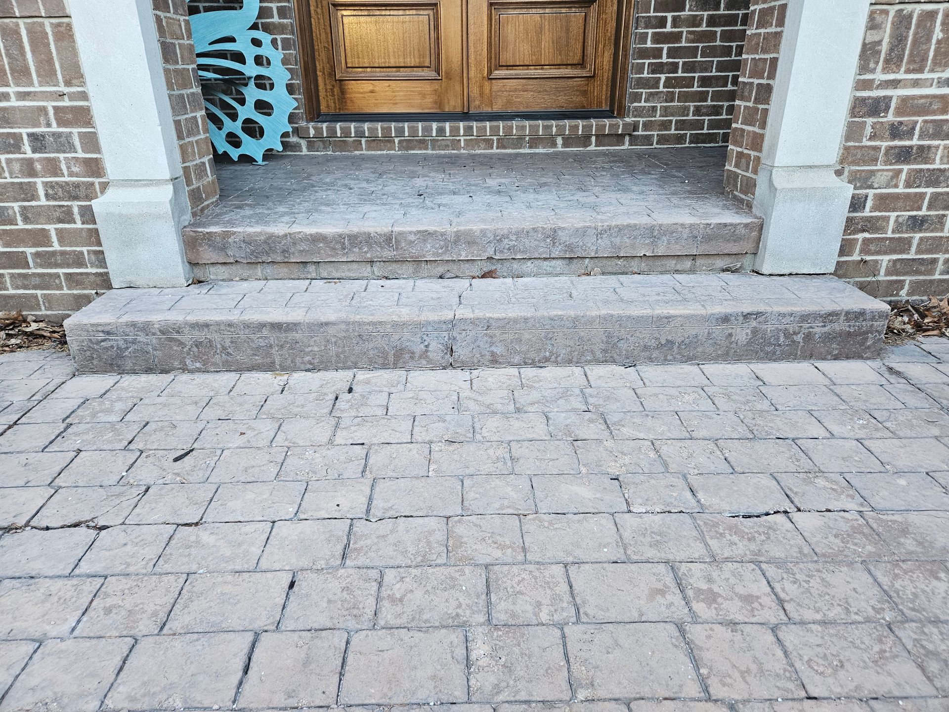 Stone walkway leading to a wooden front door with brick steps and a blue gear decoration on the left