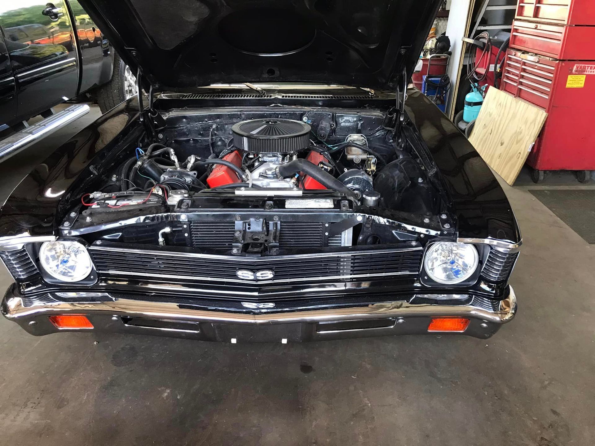 A black car with the hood up is parked in a garage.