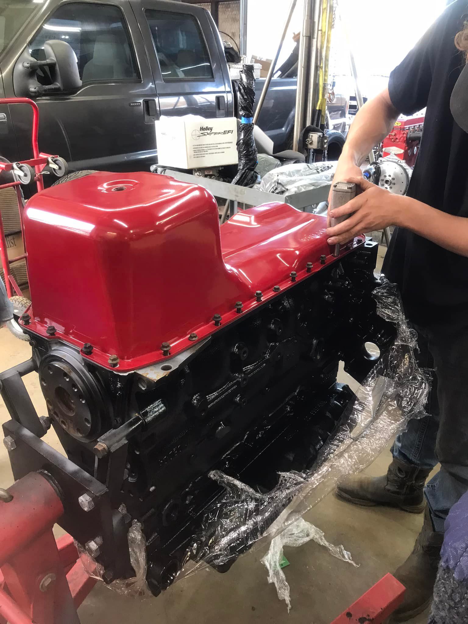 A man is working on a red engine in a garage.