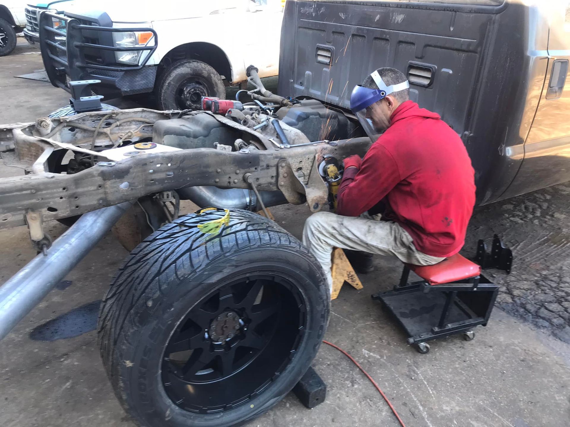 A man in a red jacket is welding a truck frame