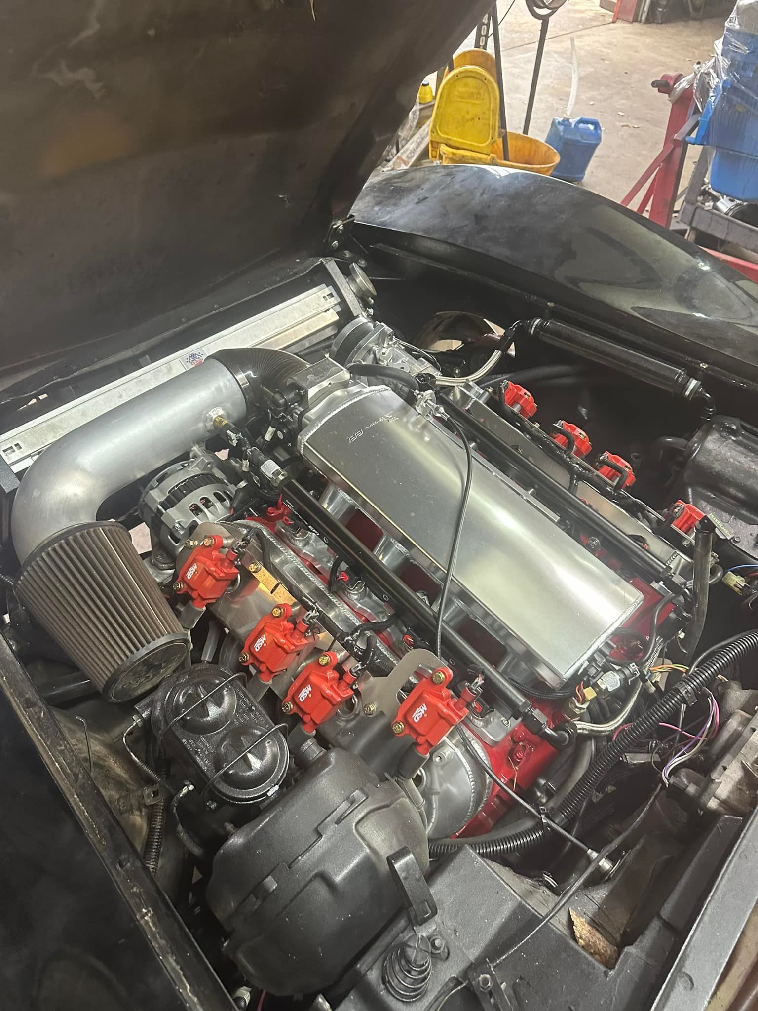 A close up of a car engine with the hood open in a garage.