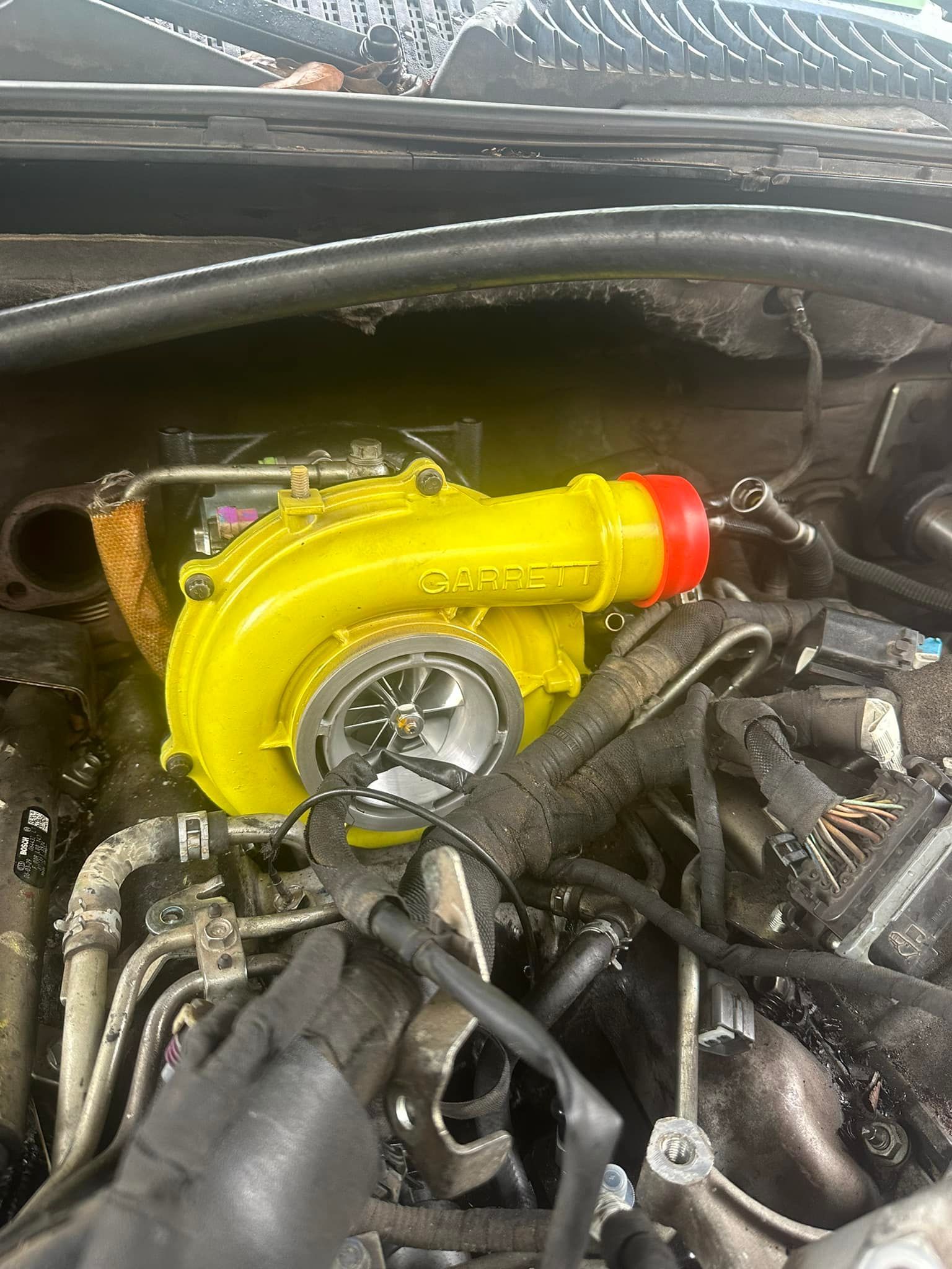 A yellow turbocharger is sitting inside of a car engine.