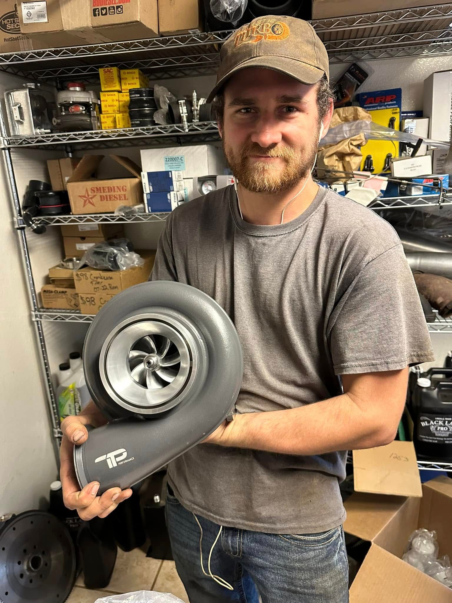 A man is holding a turbocharger in his hands in a garage.
