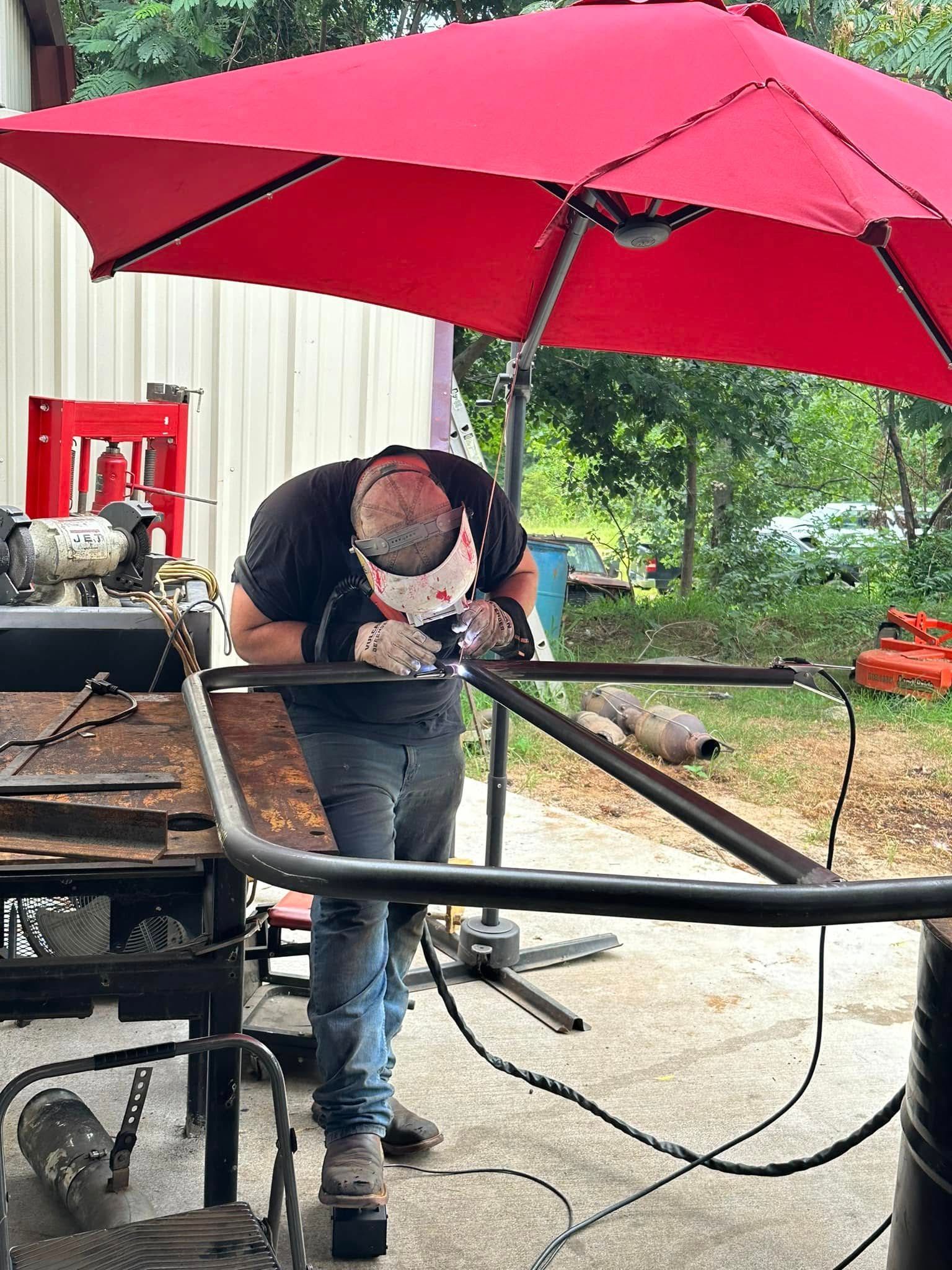 A man is welding a piece of metal under an umbrella.