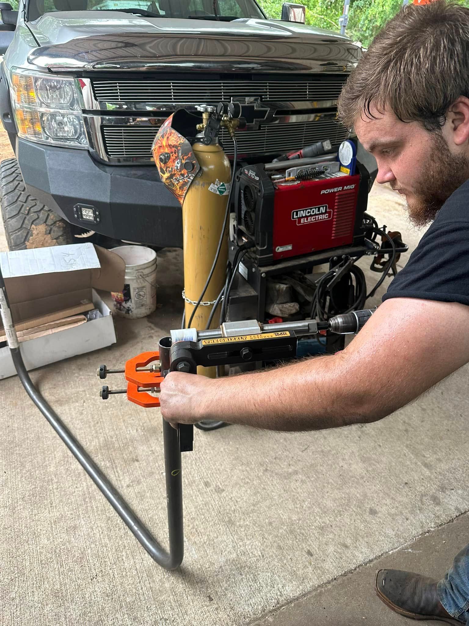 A man is welding a pipe in front of a truck.