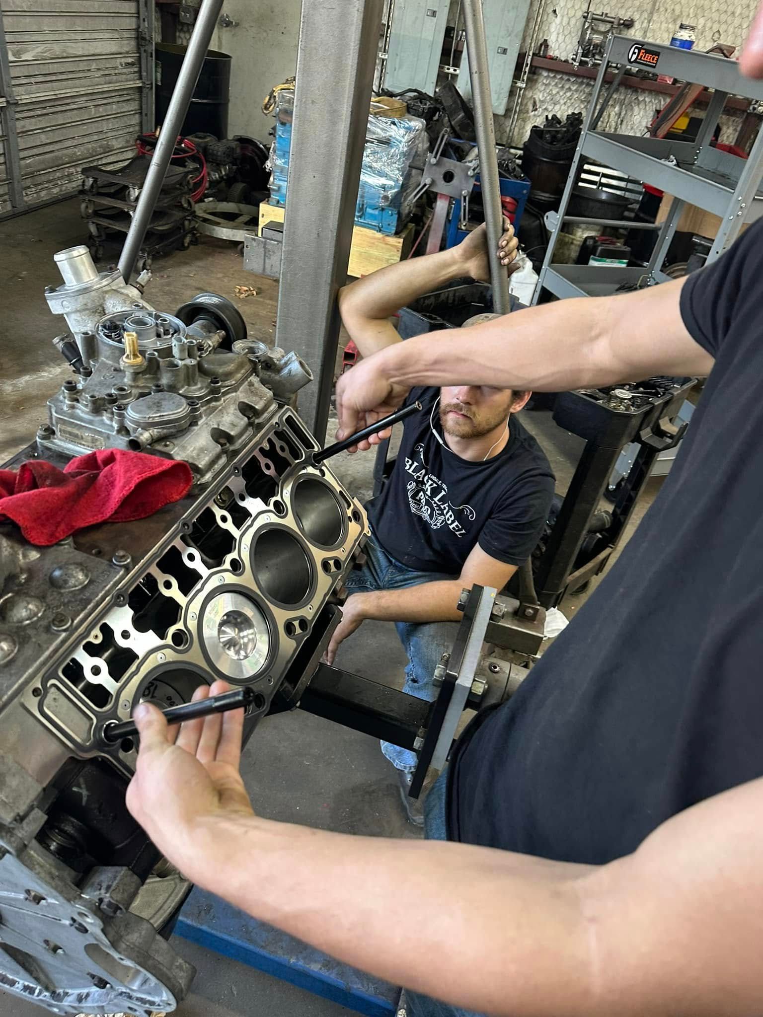 Two men are working on a car engine in a garage.
