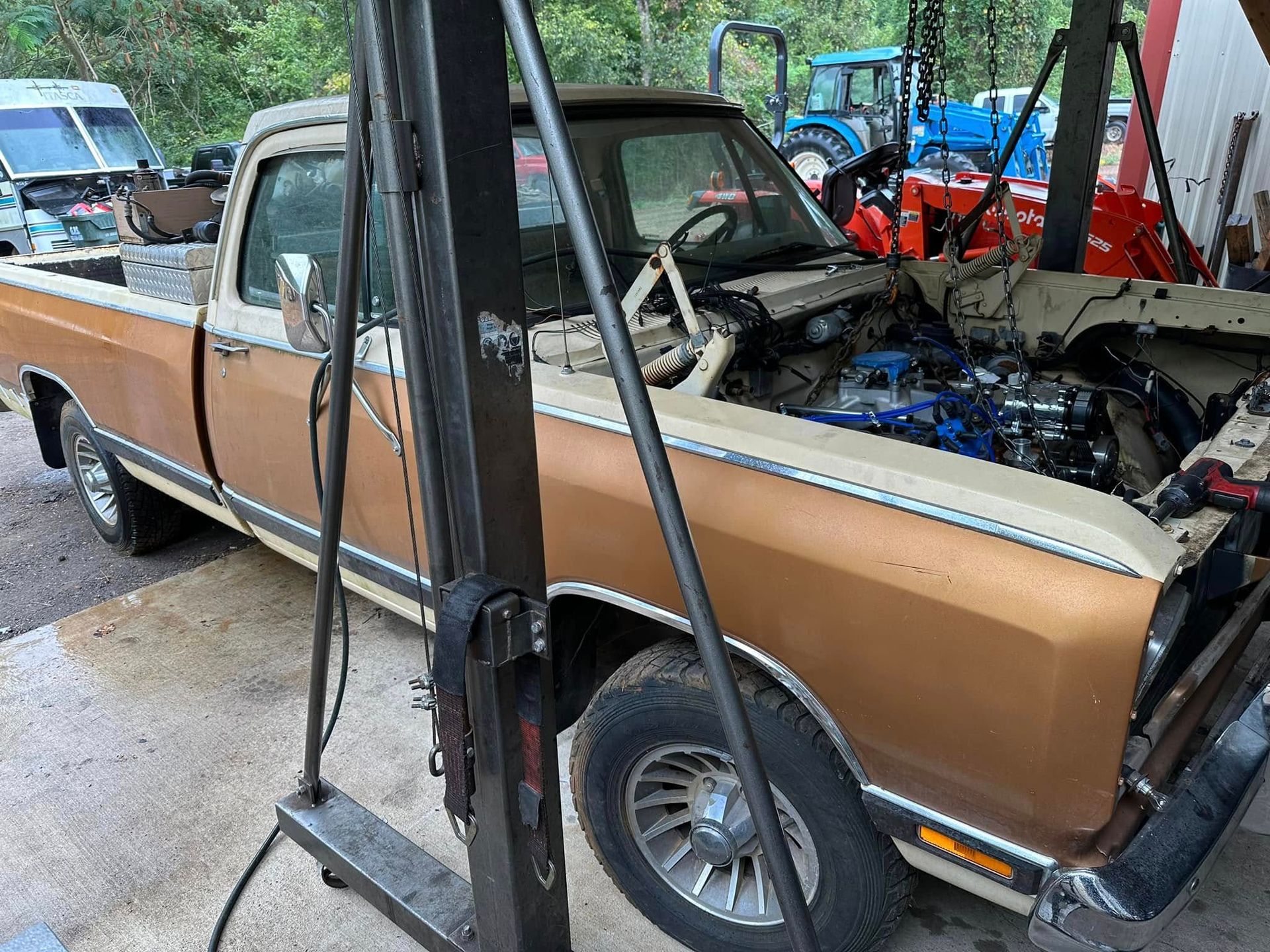 A brown truck with the hood open is sitting on a lift.