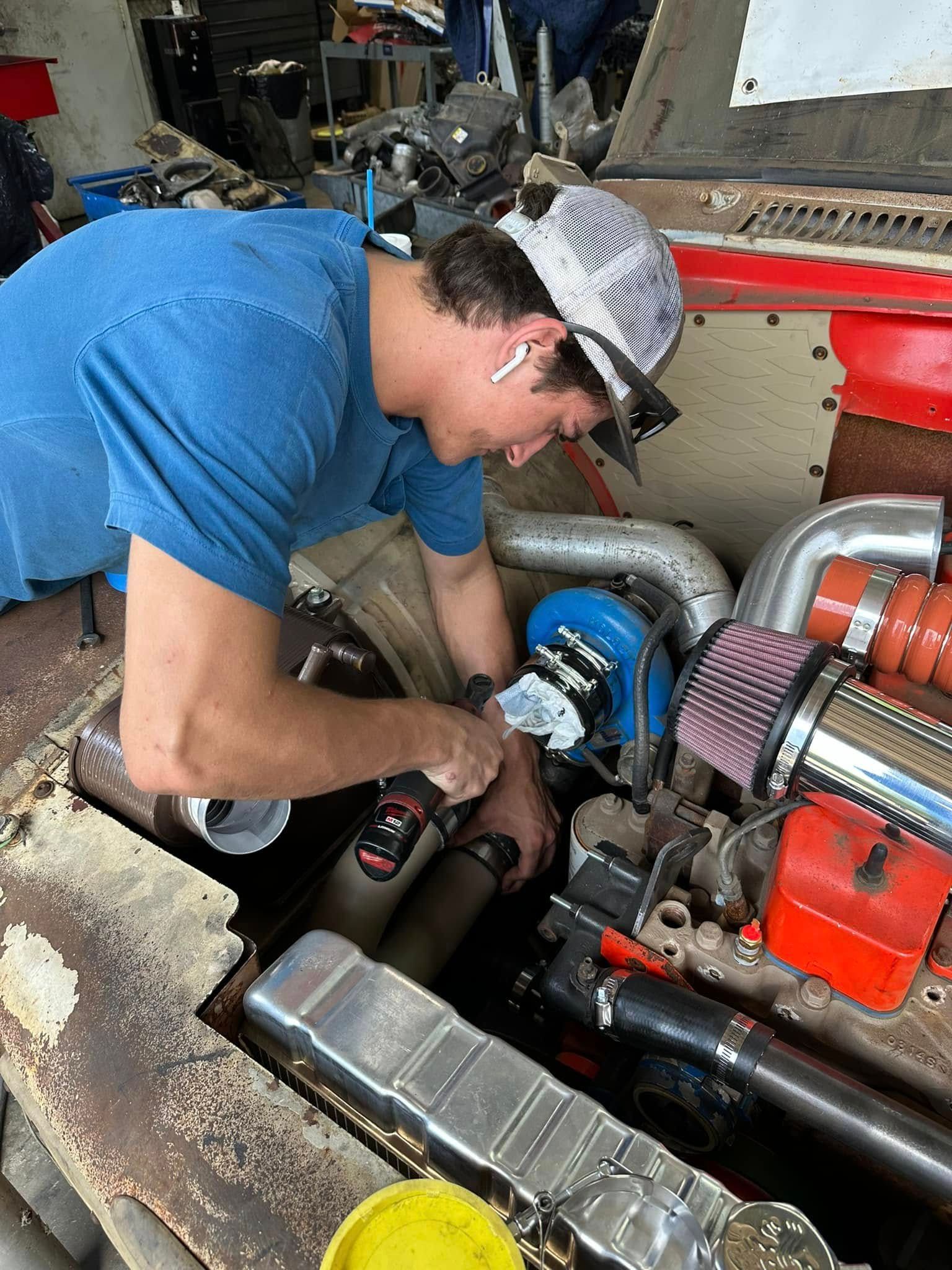 A man is working on a car engine with a drill.