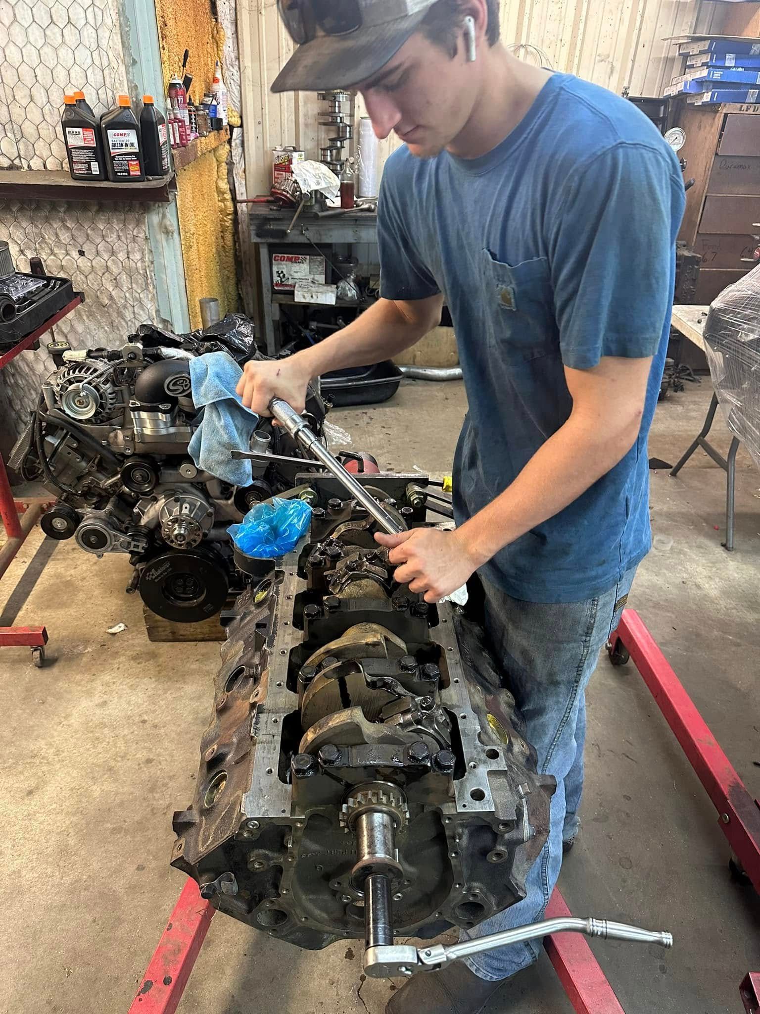 A young man is working on a car engine in a garage.
