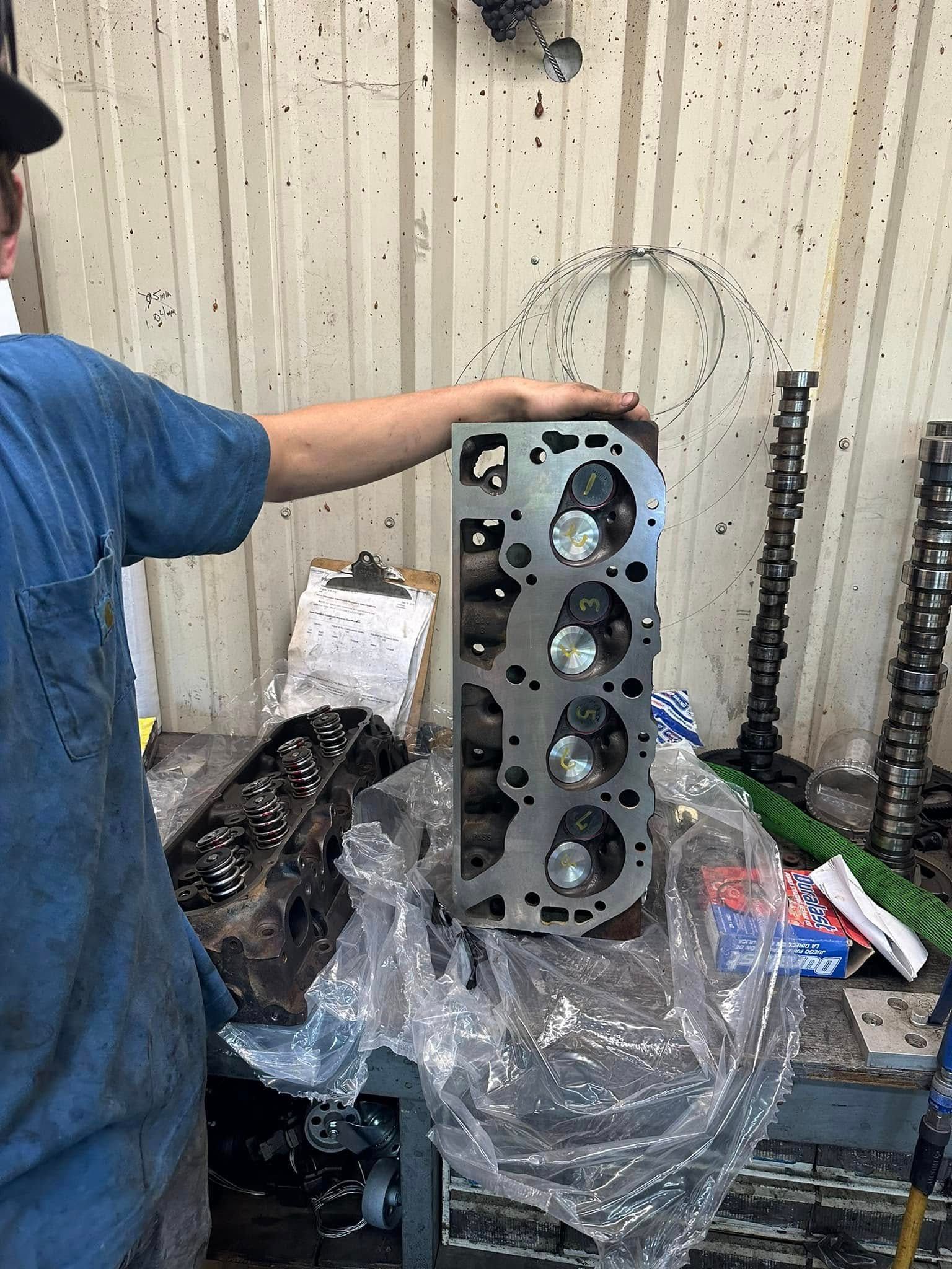 A man is working on a cylinder head in a garage.
