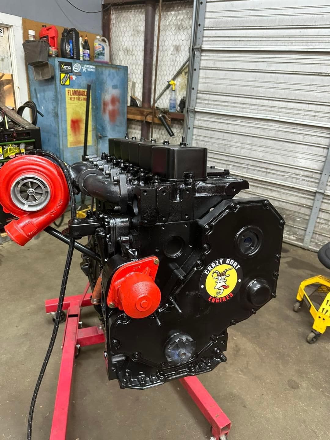 A black engine is sitting on a red stand in a garage.