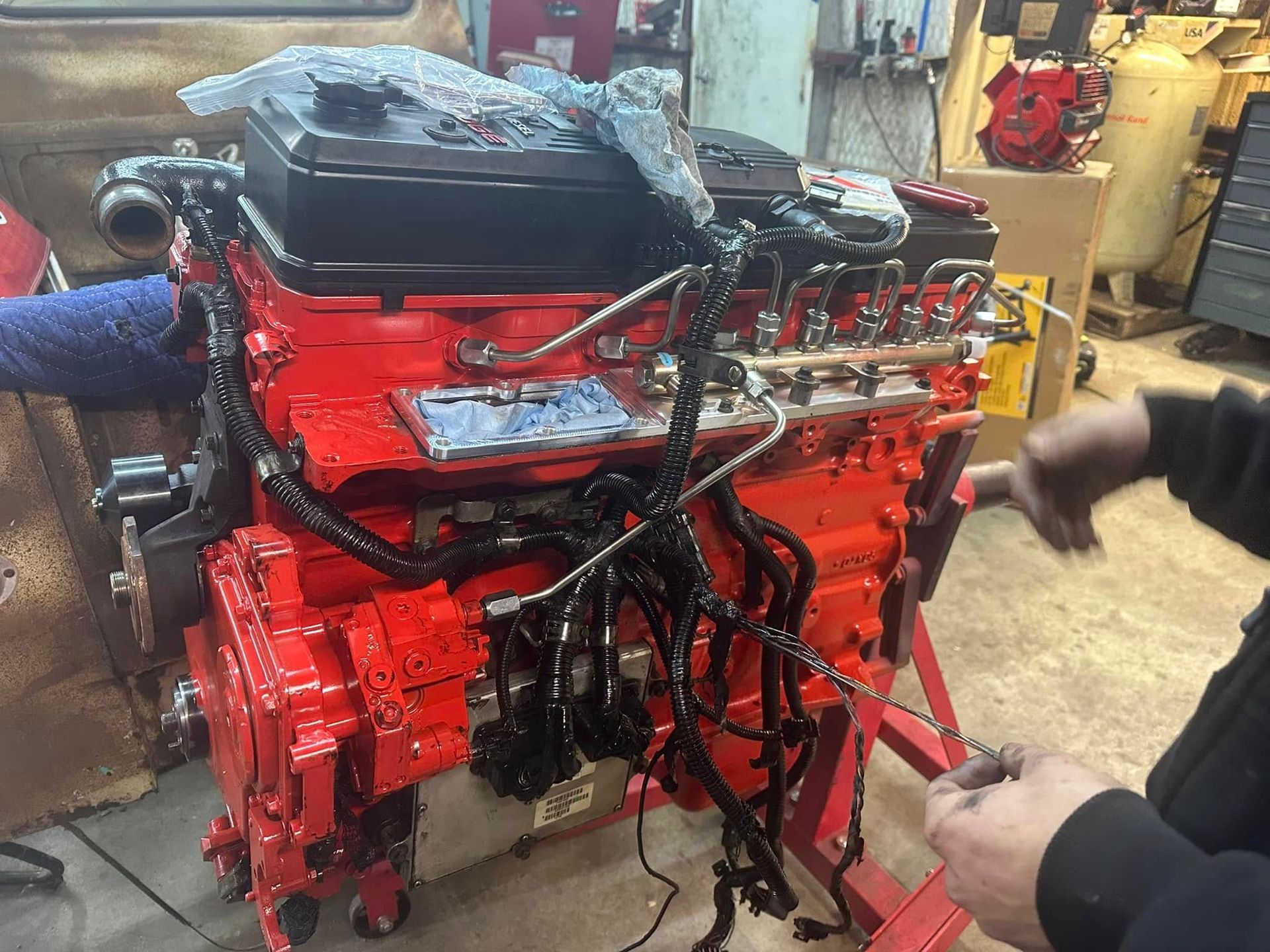 A man is working on a red engine in a garage.