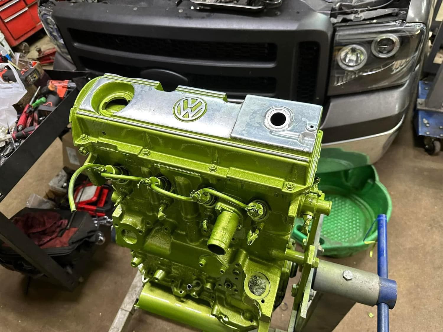 A green engine is sitting on a stand in front of a car.
