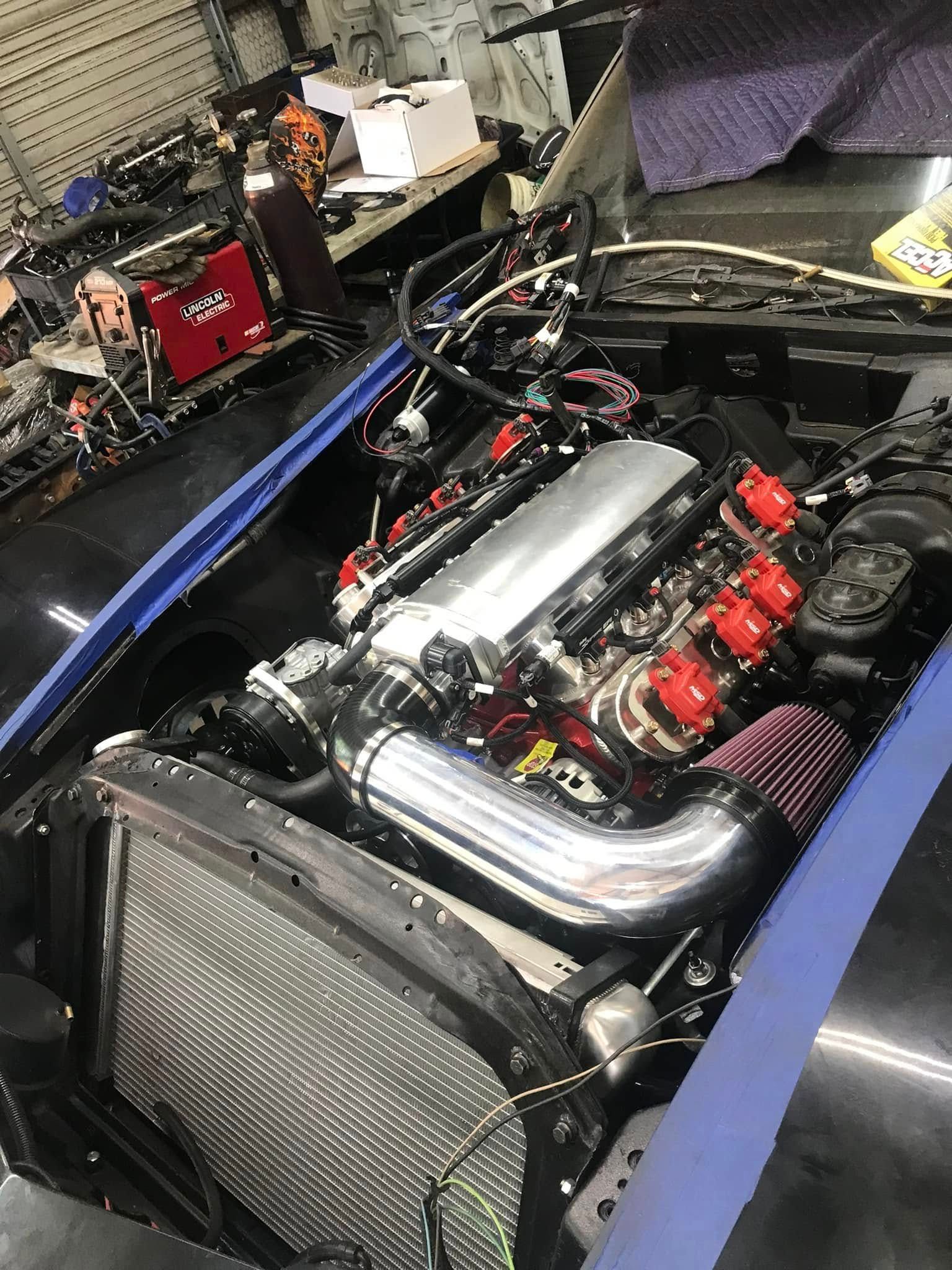 A close up of a car engine with the hood open in a garage.