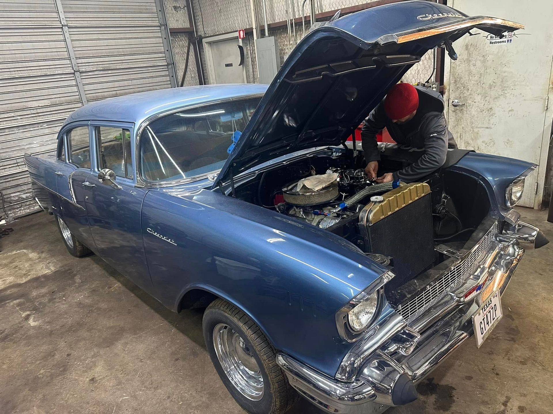 A man is working on an old blue car with the hood open.