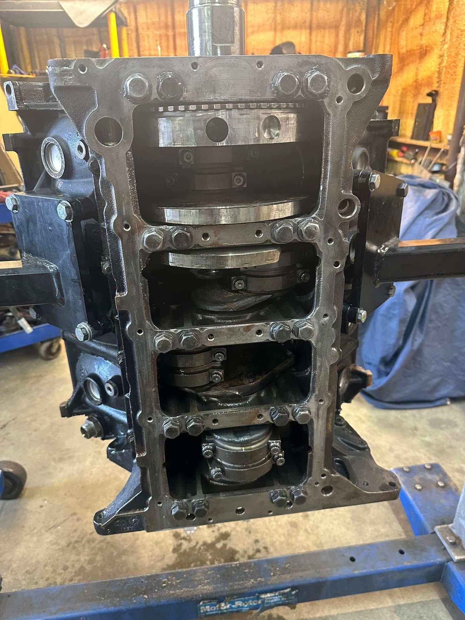 A black engine block is sitting on top of a blue stand in a garage.