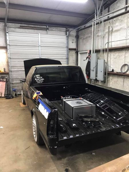 A black truck with the hood up is parked in a garage.