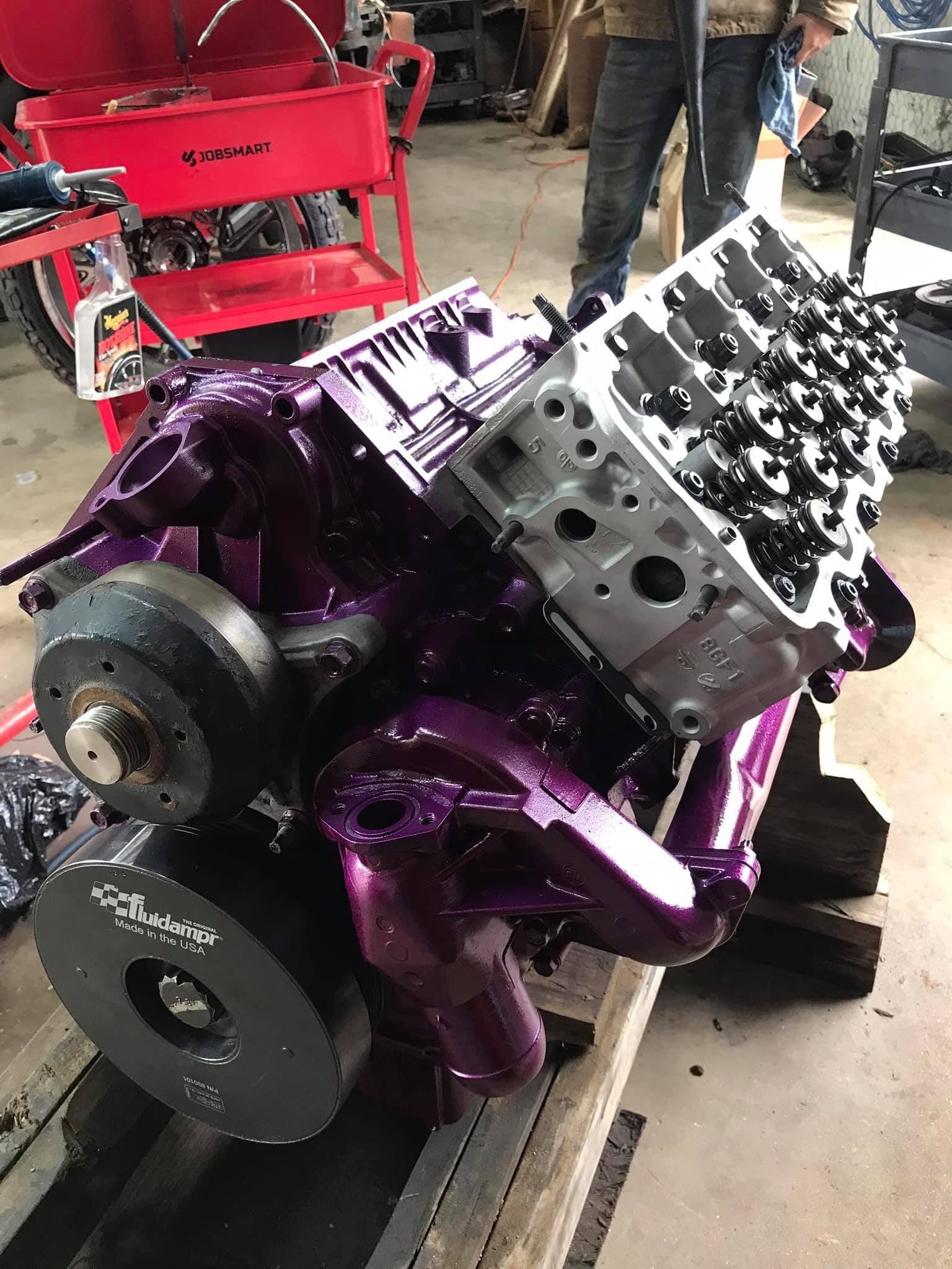 A purple engine is sitting on top of a wooden table in a garage.